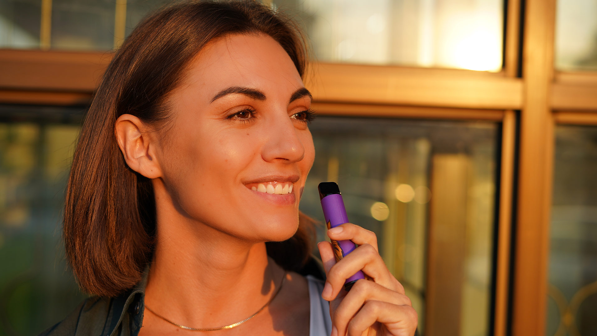 Donna sorridente che utilizza una penna sigaretta elettronica all'aperto al tramonto, raffigurante lo stile di vita della riduzione del consumo di nicotina attraverso il vaping.