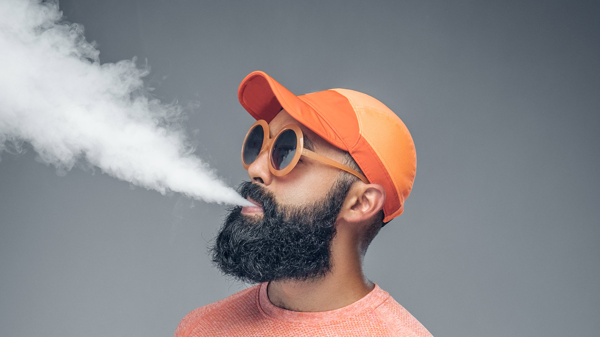 Un uomo con cappello e occhiali arancioni che svapa.